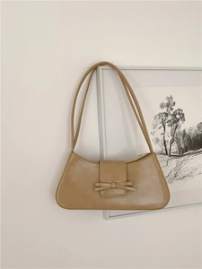 Khaki leather baguette bag with bow detail hanging against a minimalist white wall