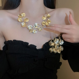 Close-up of golden leaf-shaped necklace and earring set worn on model with soft lighting