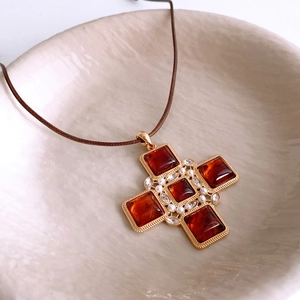 Detail of vintage gold cross pendant with amber resin, pearls and crystals on leather cord