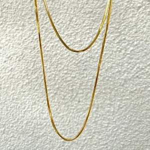 Double-layered golden snake chain necklace in stainless steel on a white textured background