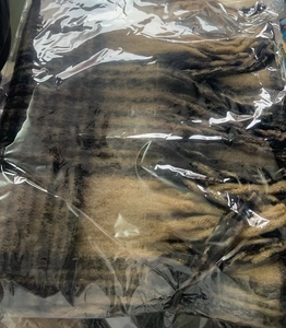 Detail view of brown and beige striped knit scarf with tassels in clear packaging