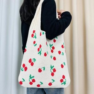 Close-up of knit tote bag featuring red cherry patterns and green leaves on cream fabric