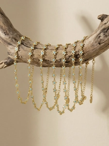 Close-up of golden necklace with light blue flowers hanging on a natural wooden branch