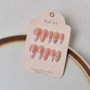 Macro detail of nude press-on nails with 3D flowers and pearls on display card