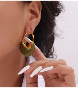 Detailed close-up of golden asymmetric hoop earrings with olive green enamel pendants