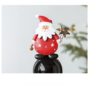 Detail of Santa Claus wine bottle topper with golden bells against a festive tree