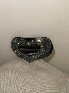 Dettaglio di un fermaglio a cuore con strass scuri e una perla grigia dallo stile retrò