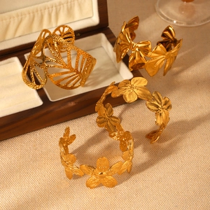 Dettaglio di bracciali rigidi placcati in oro 18K con trame di fiori, farfalle e foglie