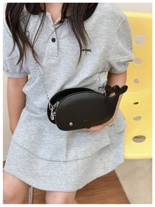 Kid's black whale-shaped crossbody bag with silver chain worn by a model in a grey dress