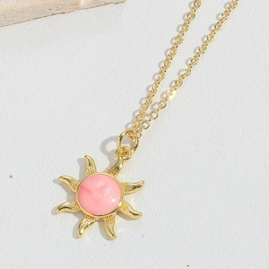 Detailed macro view of the gold sun pendant with pink enamel center on a slim chain