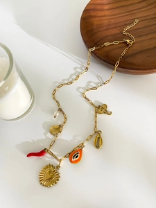 Detail of 18K gold necklace with diverse charms like heart, chili, and shell on a white surface