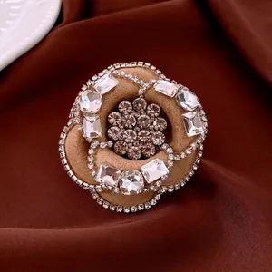 Elegant camellia flower brooch with beige flocking and sparkling rhinestones on dark fabric