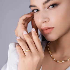 Detail of gold heart-shaped ring with inlaid stones on model's hand with matching necklace