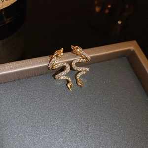 Elegant gold zodiac dragon earrings with shimmering zircons on a gray jewelry box edge