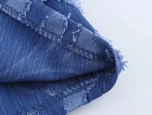 Close-up of blue denim fabric with raw edges and detailed stitching on the garment