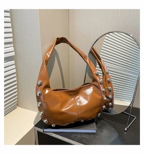 Close-up of brown glossy oil-wax leather handbag featuring bold silver rivet decorations