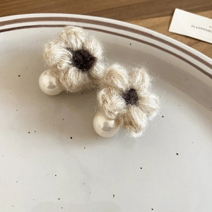 Detail view of knitted flower stud earrings with pearl on a vintage ceramic plate