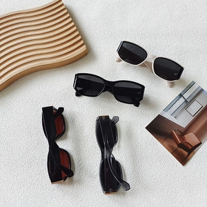 Retro rectangular sunglasses in black and cream beige, displayed on artistic white texture