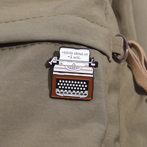 Detail of vintage typewriter enamel pin with creative quote on a canvas backpack strap