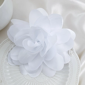 Close-up of white silk fabric flower brooch with layered petals on a textured white plate