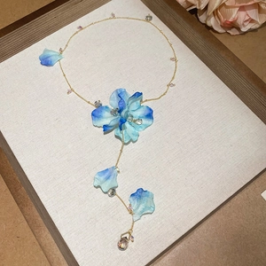 Detailed shot of a gold necklace featuring blue fabric petals and crystal flower accents