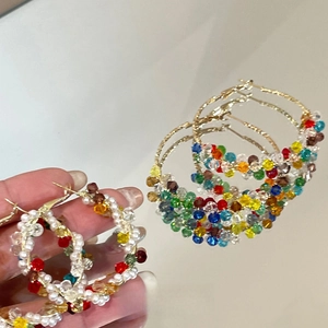 Close-up of colorful beaded C-shaped hoop earrings with pearls and crystals on gold metal