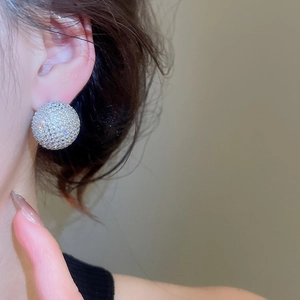 Close-up of a large spherical silver stud earring with pavé-set cubic zirconia on a model