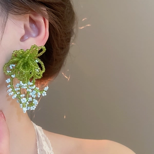 Close-up of model wearing handmade green beaded flower earrings with fringe detail