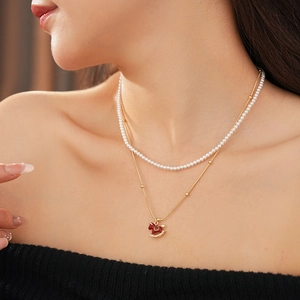 Close-up of a double-layered necklace with pearls and a red enamel rocking horse pendant