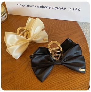 Detail view of satin bow hair claws in cream and black with gold LOVE DAYS metal charms