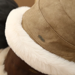 Détail du bob en daim camel avec bord en fausse fourrure blanche et plaque logo en métal
