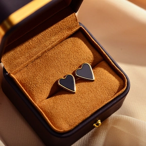 Close-up of heart-shaped black enamel earrings with gold trim in a premium jewelry box