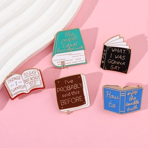 Collection of five book-shaped enamel pins with witty quotes on a soft pink background