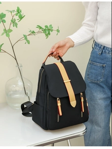 Detail of black oxford backpack showing beige leather handle and golden metal zippers