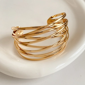 Close-up of golden multi-layer crisscross open bangle on a white ceramic plate