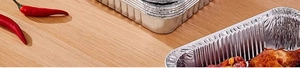 Close-up of rectangular aluminum foil containers with fried chicken on wood surface