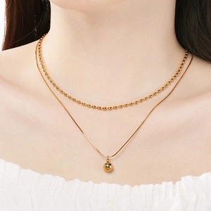 Détail d'un collier double épaisseur en acier inoxydable avec un pendentif boule dorée
