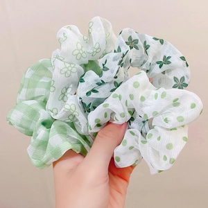 Detail of green scrunchies featuring checkered, floral, and polka dot patterns on soft fabric