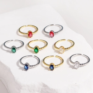 Flat lay of adjustable open rings with colorful oval gemstones on white stone background