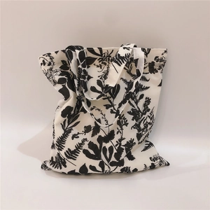 Detailed view of white canvas tote bag with black leaf silhouette patterns and soft shadows
