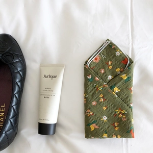 Flat lay of a green floral cotton scarf next to a black quilted flat shoe and hand cream