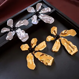 Exaggerated metal flower earrings in gold and silver finish on black display tray