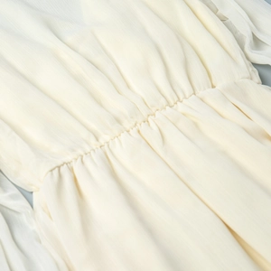 Detailed close-up of smocked waist and ruffled texture on cream chiffon dress