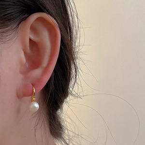 Close-up of elegant white freshwater pearl earrings with golden hooks worn on the ear