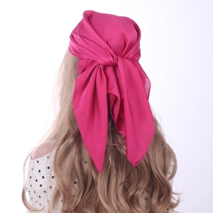 Detail of rose red satin square scarf tied as an elegant hair accessory on model