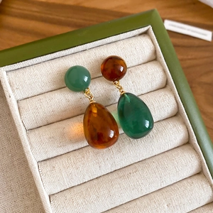 Detailed view of asymmetric water-drop resin earrings in vintage green and amber hues