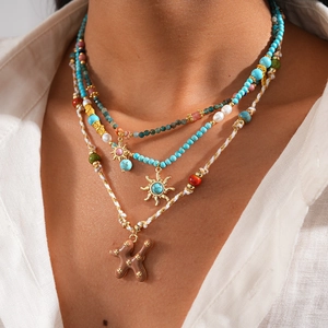 Détail de colliers en perles de turquoise avec pendentif soleil doré sur une chemise