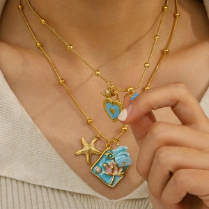 Gold layered necklace featuring blue enamel heart and starfish charms for beach style
