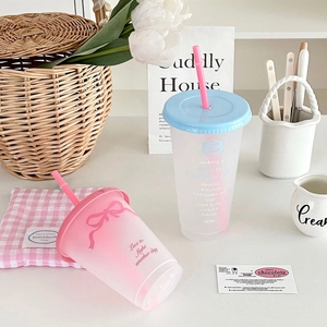 Pastel plastic tumblers with straws and bows on a cozy aesthetic tabletop display