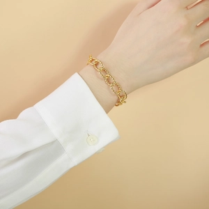 Macro detail of gold-plated twisted rope chain bracelet on white shirt sleeve